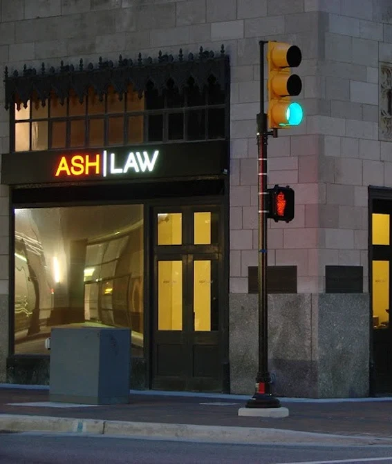 Exterior of a Ash law office with illuminated 'ASH | LAW' sign at dusk, featuring a green traffic light and pedestrian stop signal