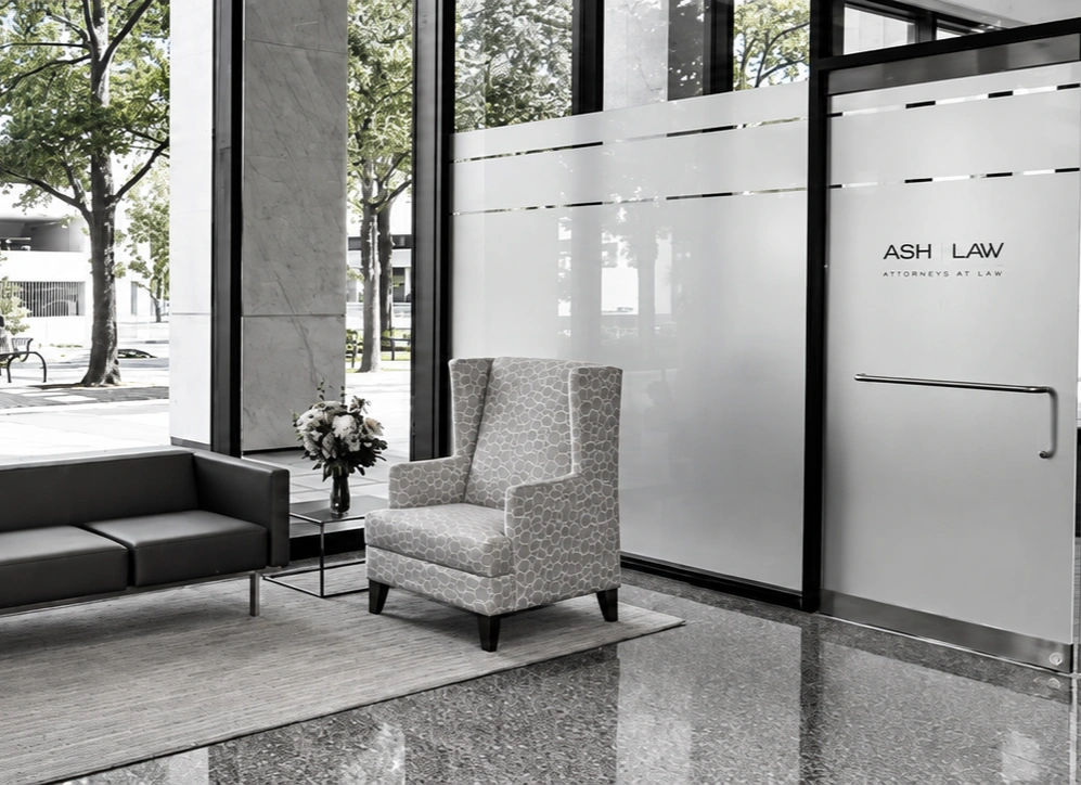 Modern office waiting area with a sofa, armchair, glass coffee table with flowers, and large windows overlooking an outdoor scene