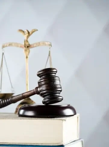Wooden judge's gavel on a book with brass scales of justice in the background, symbolizing law and legal authority