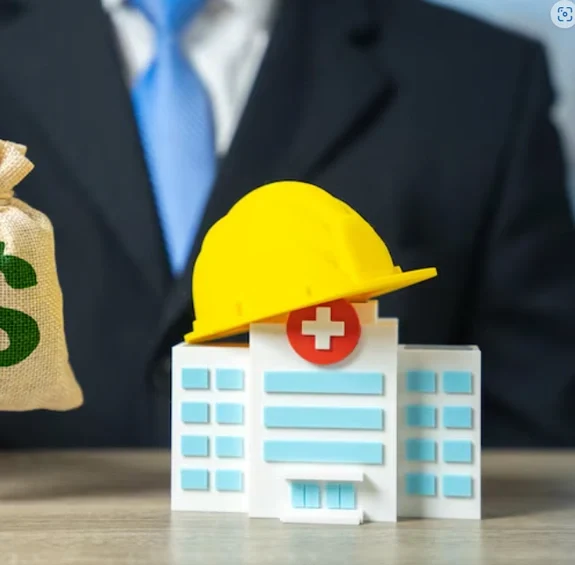 Model of a hospital building wearing a yellow hard hat, next to a person in a suit holding a money bag with a dollar sign